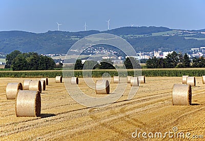 Straw bales in the field with the city and wind turbines in the background. Stock Photo