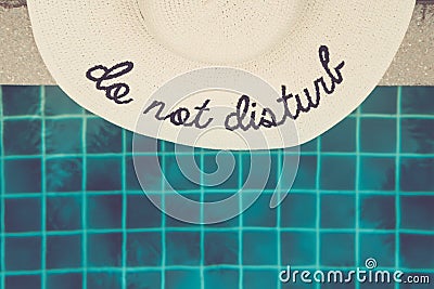 Straw hat with Do not disturb wording at the pool edge Stock Photo