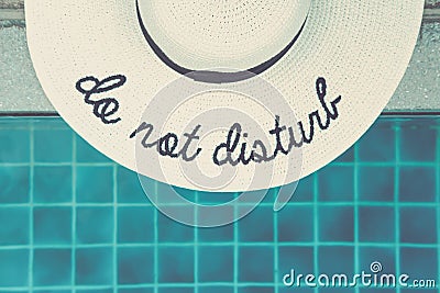 Straw hat with Do not disturb wording at the pool edge Stock Photo