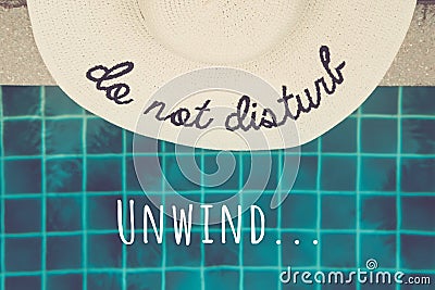 Straw hat with Do not disturb wording at the pool edge with Unwind... wording Stock Photo