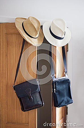 Straw hats and leather handbags hanging from a door with window natural light. Stock Photo