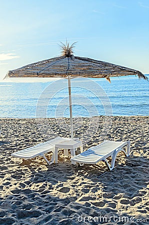 Straw sun umbrellas and white plastic sunbeds, beach with sand n Stock Photo
