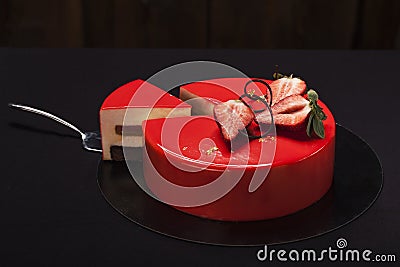 Strawberry cake covered with red mirror glaze decorated with berry pieces, gold and chocolate. A modern cake with a cut piece Stock Photo