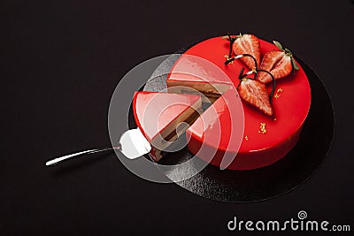 Strawberry cake covered with red mirror glaze decorated with berry pieces, gold and chocolate. A modern cake with a cut piece on b Stock Photo