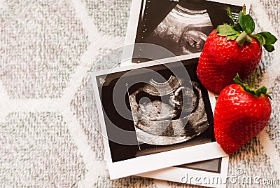 Strawberry and photos of a human fetus from ultrasound scan during pregnancy on right side gray background Stock Photo