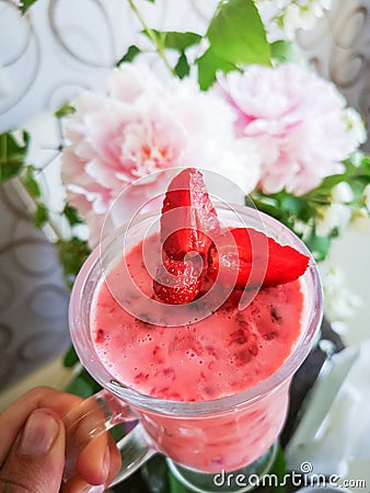 Strawberry smoothie in the hand of a girl. Woman drinking a pink cocktail with berries, a cocktail against the Stock Photo