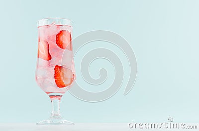 Strawberry water with red fruit slices, ice cubes, sparkling water in misted glass in modern mint color interior. Stock Photo