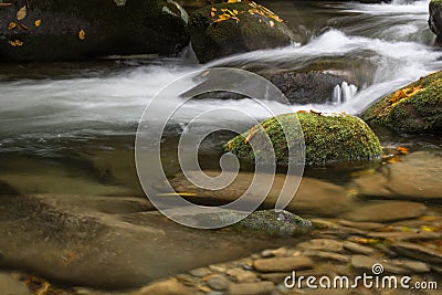 Stream with surface and submerged rocks with moss and fall leaves Stock Photo