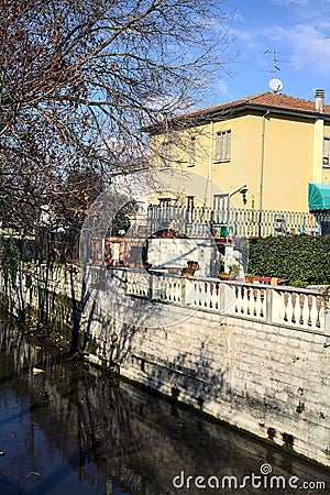 Stream of water next to a group of houses and bordered by bare trees on a sunny day in winter Stock Photo