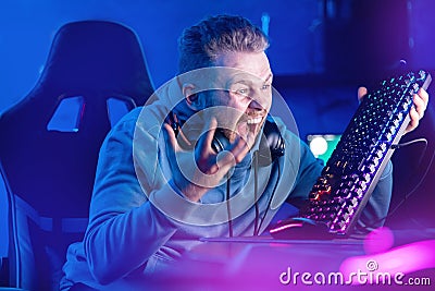 Streamer Angry computer gamer man yells and breaks keyboard after being defeated in online video game Stock Photo