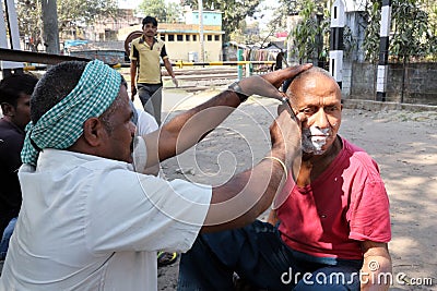 Street barber shaving a man on a street in Kolkata Editorial Stock Photo