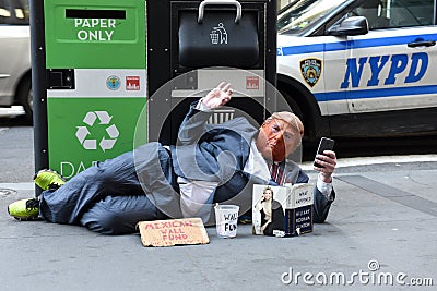 Street beggar wears a Trump mask and reading the book of Hillary Clinton What Happened. Editorial Stock Photo