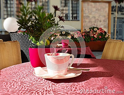 Street Cafe on table cup of coffee and pink flowers pink coral tablecloth on the table and yellow chair cloth morning breakfast Stock Photo