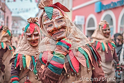 Friendly carnaval figure in brown, green, red robe shows hand gesture. Carnival in southern Germany - Black Forest Stock Photo