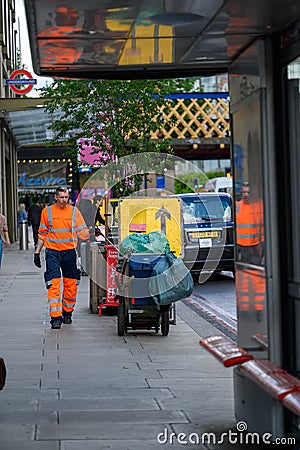 Street cleaner in orange reflective clothing with dust cart outside Waterloo Station Editorial Stock Photo