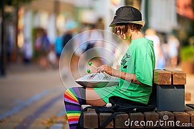 Street hank drum musician, young girl sitting on street bench and playing music on steel tongue drum Editorial Stock Photo