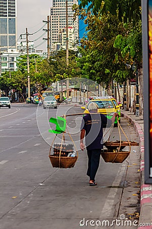 Street hawker is walking with carry bamboo baskets of grilled eggs on shoulder pole go around Bangkok, Thailand. Editorial Stock Photo