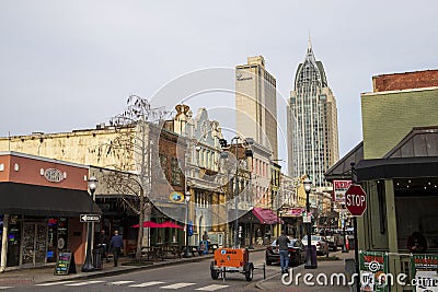 A street lined with shops and restaurants with tall black light posts and cars on the street and people on the sidewalk Editorial Stock Photo