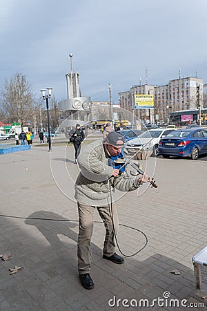 A street musician playing a musical instrument in front of a parking lot. A mature man with an electronic violin. Black baseball Editorial Stock Photo