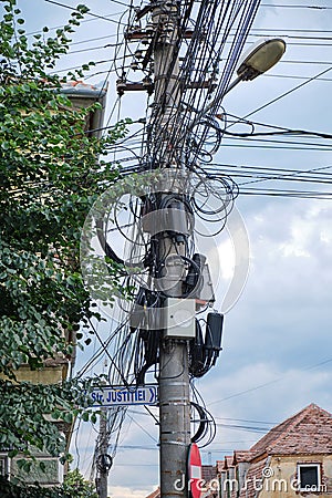 Street pole with TV, internet, telephony, and electricity cables hanging from it in an unorganized matter Stock Photo