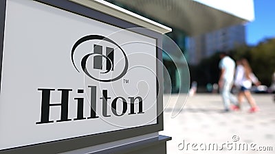 Street signage board with Hilton Hotels Resorts logo. Blurred office center and walking people background. Editorial 3D Editorial Stock Photo