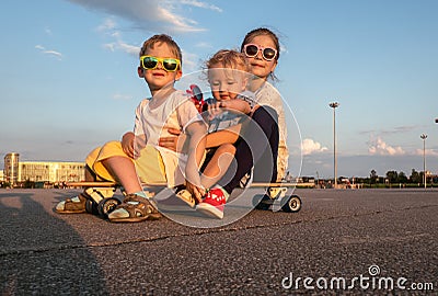 Street sports: A boy and two girls in sunglasses sit together on a large longboard. The summer solchechny frame. Stock Photo