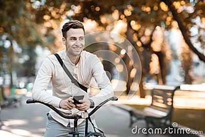 Street style. Young stylish man texting on phone while sitting on bike Stock Photo