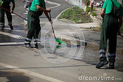 Street sweeper cleaning city sidewalk with water from a hose and a plastic broom - blue collar jobs Stock Photo