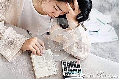 Stress Asian woman calculating her debt having problem with loan looking at list of expenses on notepad with invoices on floor Stock Photo
