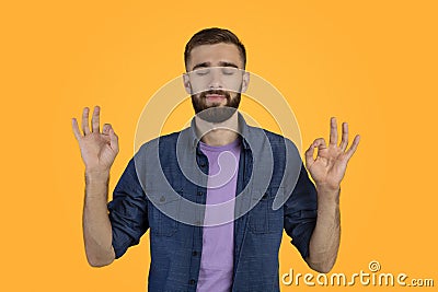 Stress relief concept. Handsome young man meditating with closed eyes, keeping calm on orange studio background Stock Photo