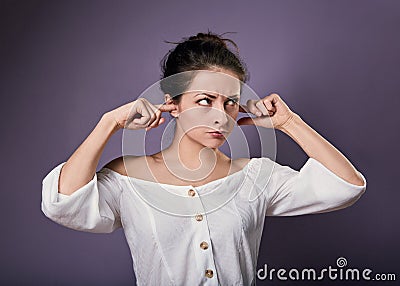 Stressed unhappy casual woman closed ears the fingers because not want the hear any sounds and noise on purple background. Closeup Stock Photo