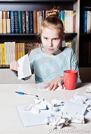 Girl angry at the table, in hands crumpling a piece of paper Stock Photo