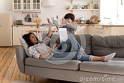 Stressed angry mom raise hand forbid noisy son to disturb her from laptop computer. Work from home Stock Photo