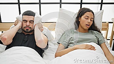 Stressed beautiful couple covering ears from noisy snore, lying together in bed, worried about sleep issue in their bedroom Stock Photo