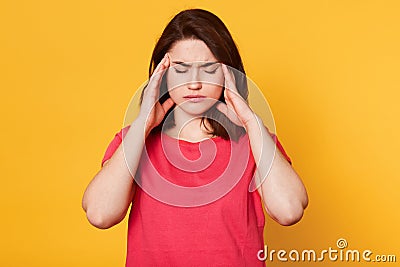 Stressed beautiful woman wears casual t shirt, touching temples and has terrible headache, attractive young lady looks tired. Stock Photo