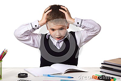 Stressed bewildered pupil sitting at the desk with hands over the head surrounded with stationery Stock Photo