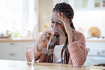 Stressed Black Lady Taking Painkiller Pill While Sitting At Table In Kitchen Stock Photo