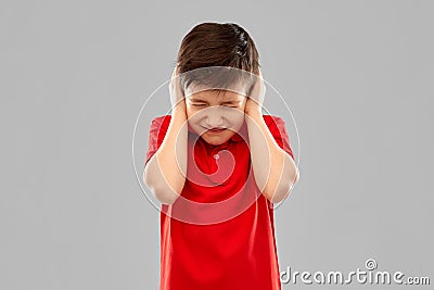 Stressed boy in red t-shirt closing ears by hands Stock Photo