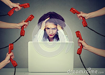 Stressed business woman working on a laptop overwhelmed by too many phone calls Stock Photo