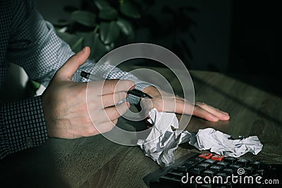 Businessman Crumpling Papers In Office. Stressed businessman with hands, sitting at workplace with crumbled papers on black shadow Stock Photo