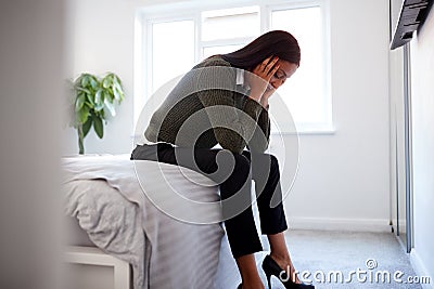 Stressed Businesswoman With Head In Hands Sitting On Edge Of Bed At Home Stock Photo