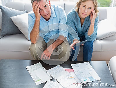 Stressed couple sitting on their couch paying their bills Stock Photo