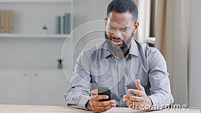 Stressed disappointed African American ethnic bearded man with mobile phone reading bad news. Office worker businessman Stock Photo