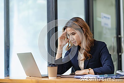 Stressed and frustrated asian female accountant sitting at desk making serious business decisions Stock Photo