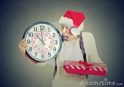 Stressed in a hurry woman wearing santa claus hat holding clock gift box Stock Photo