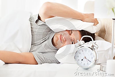 Stressed man looking at his alarm clock ringing Stock Photo