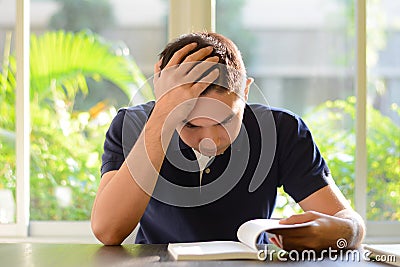 Stressed man reading book with hand on his head Stock Photo