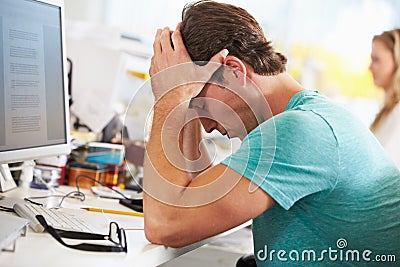 Stressed Man Working At Desk In Busy Creative Office Stock Photo