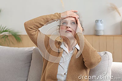 Stressed middle aged woman sit on sofa in living room, lost in thought Stock Photo