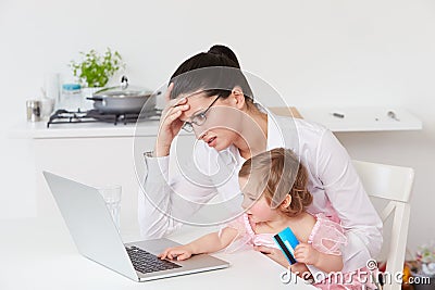 Stressed Mother With Child Using Laptop At Home Stock Photo